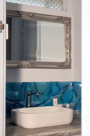 A bathroom with a white sink, a mirror with ornate silver frame, and a blue marble backsplash.