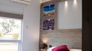 A modern hotel room with a large bed, a nightstand, an air conditioner, and two framed artworks on the wall. - Manjimup Motor Inn (Manjimup)