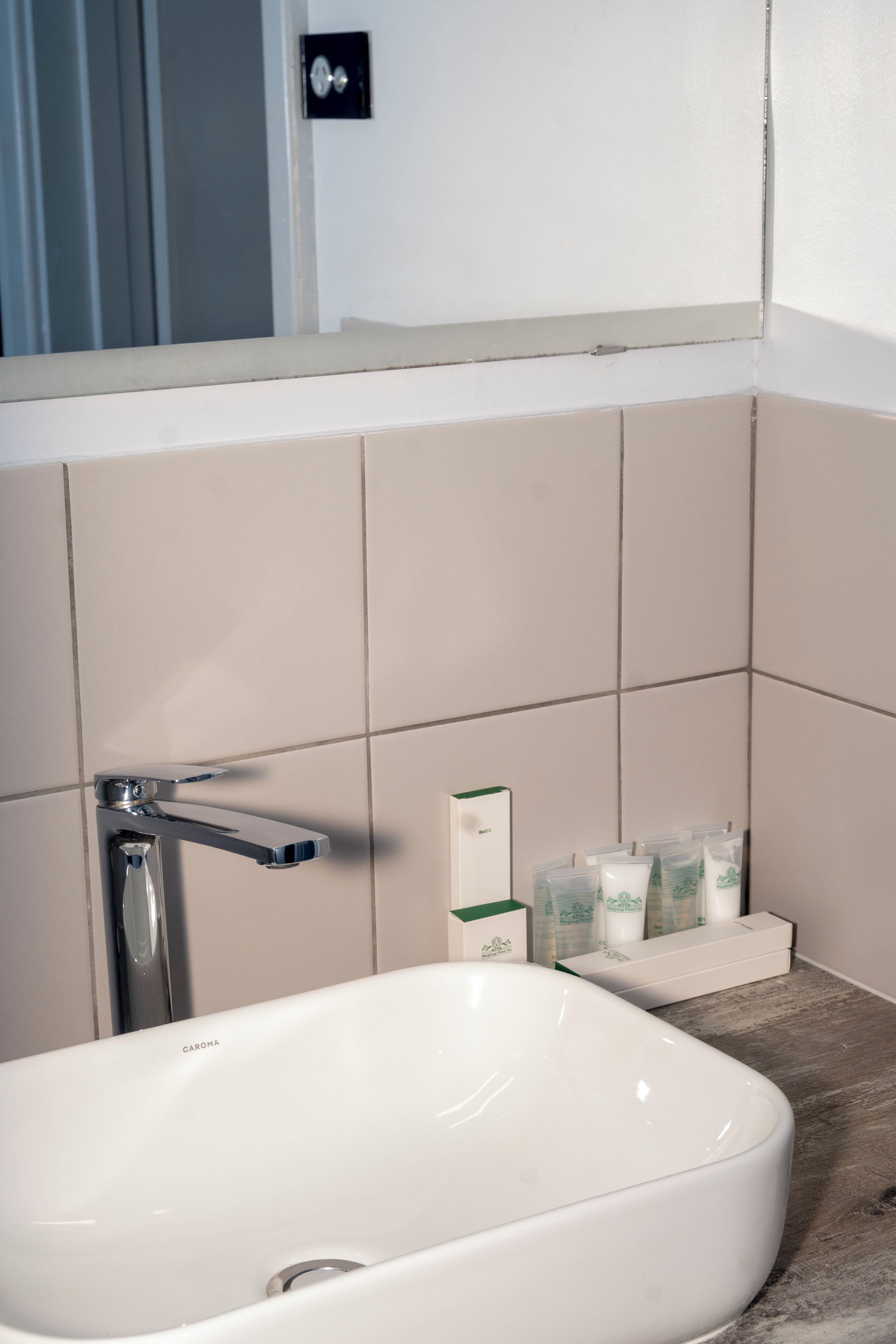Un baño con lavamanos blanco, grifo cromado y estante con artículos de aseo.