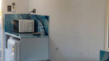 Een kleine keuken met een magnetron, een koelkastje en een glazen aanrechtblad.