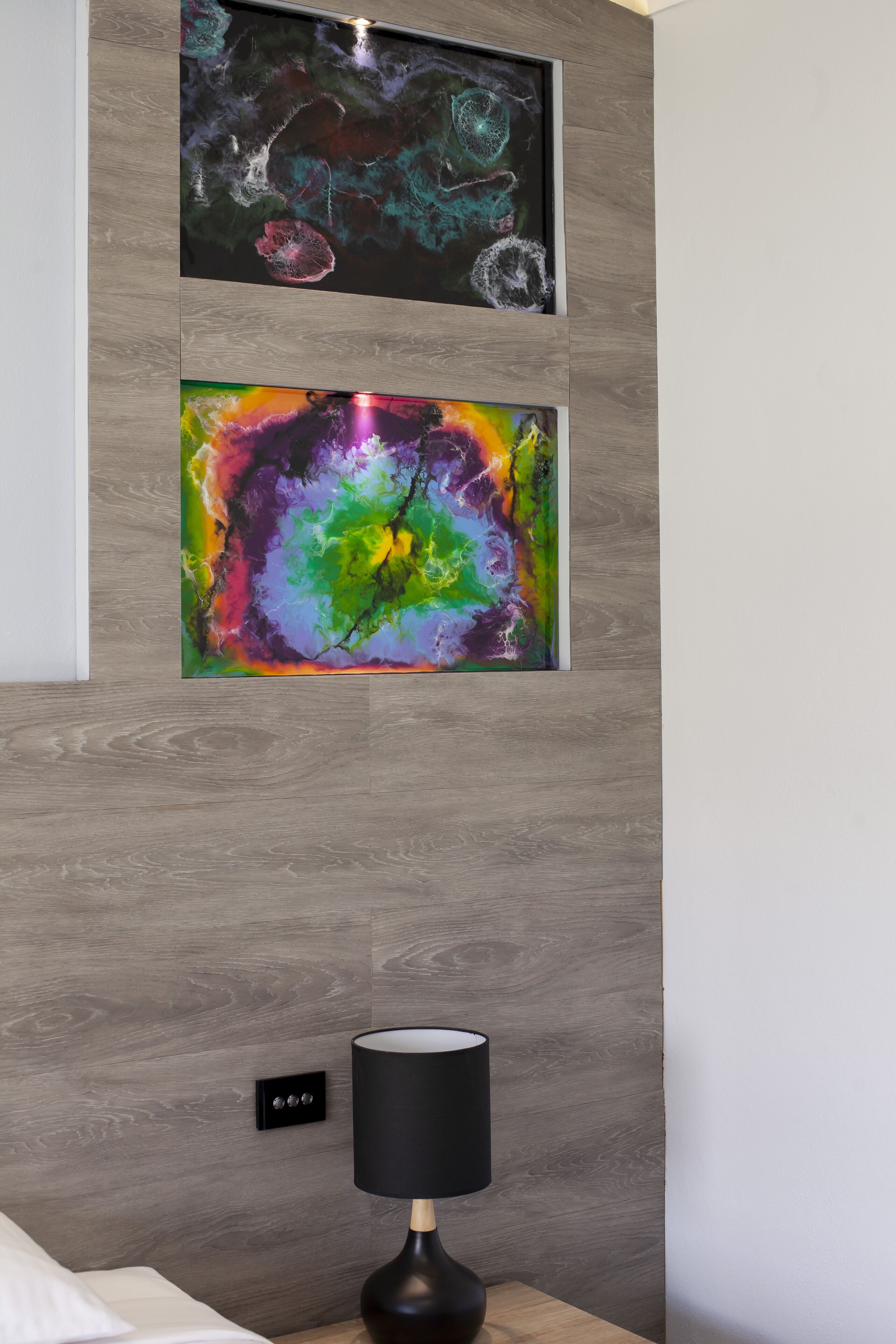 A modern room with a wooden wall, two abstract paintings, a black lamp, and a power outlet.