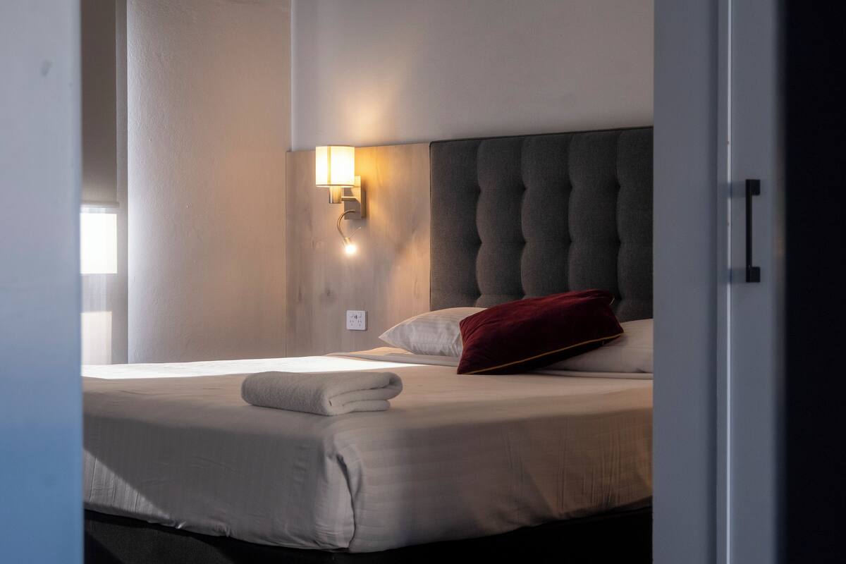 Habitació d'hotel amb un llit, una làmpada penjada a la paret i una finestra.