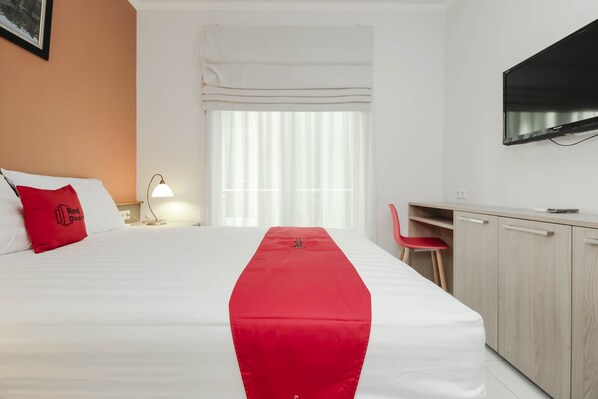 Une chambre d’hôtel avec un lit, un bureau, une télévision et une fenêtre avec des rideaux.