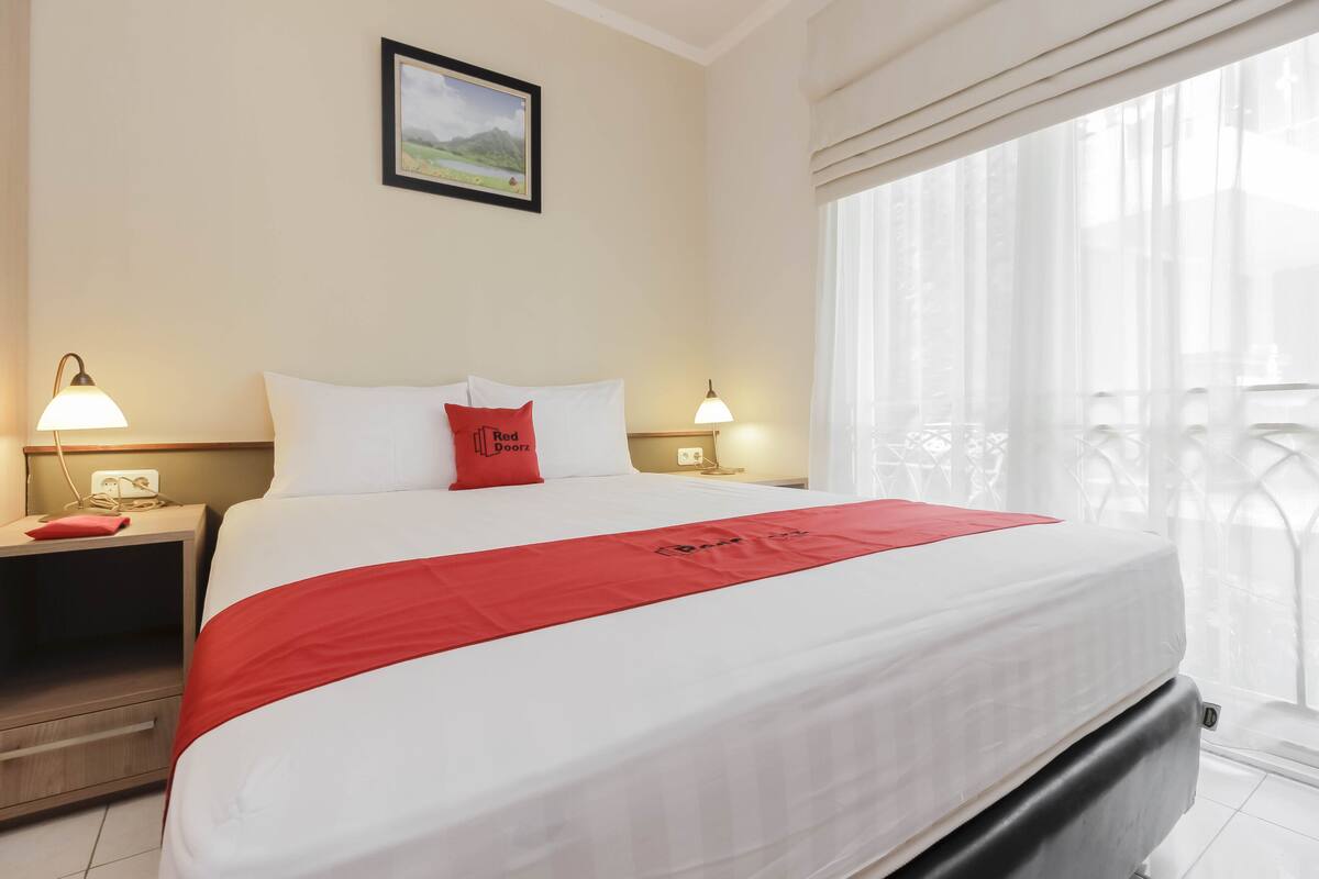 Een hotelkamer met een groot bed, twee nachtkastjes met lampen, een lijst met afbeelding aan de muur en een balkon met een hekwerk.