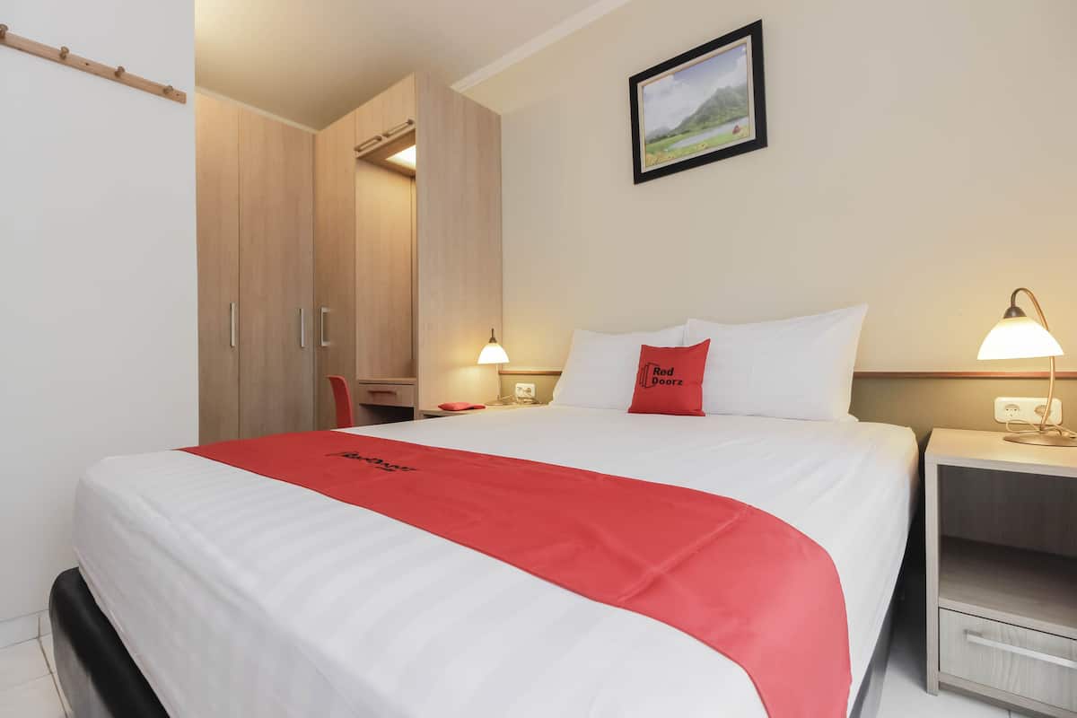 Een hotelkamer met een bed, een bureau, een stoel, een kledingkast en een nachtkastje met een lamp.