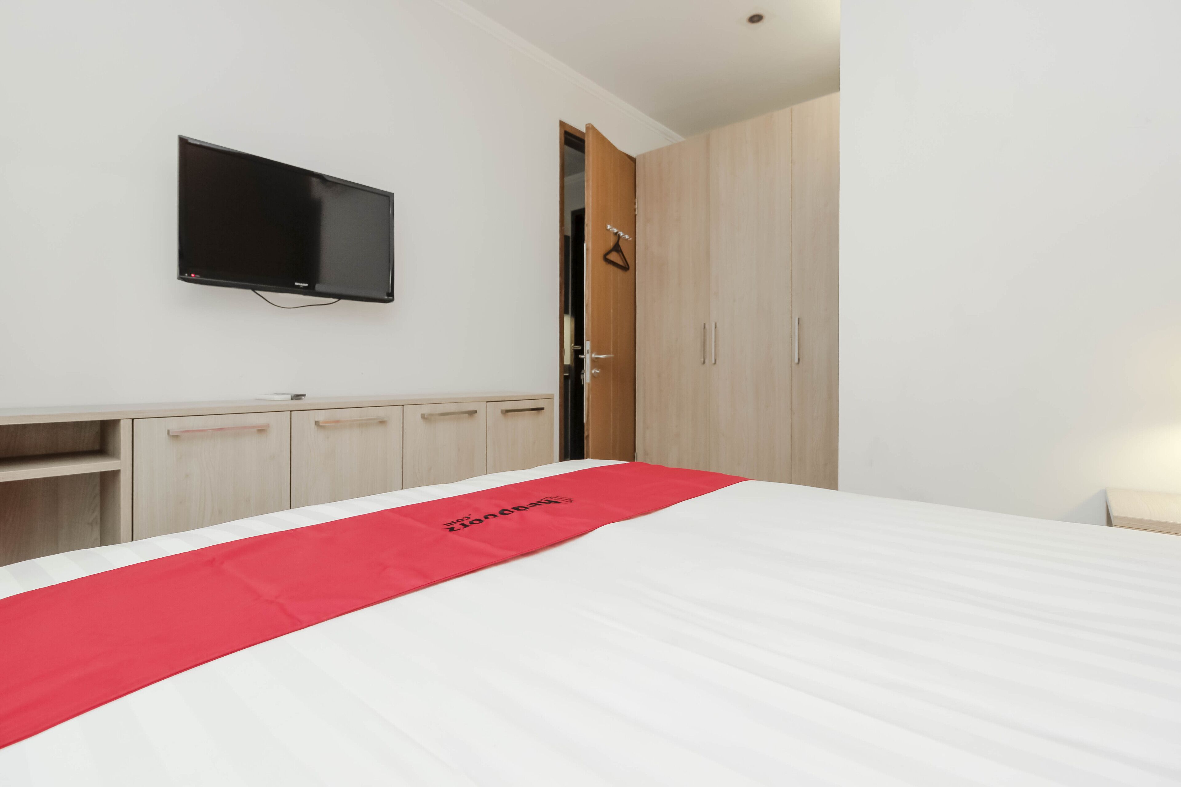A hotel room with a bed, a TV mounted on the wall, a desk, and a wardrobe.