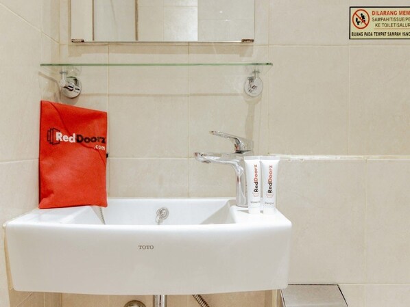 A bathroom with a white sink, a glass shelf above it, and a red bag labeled 'RedDoorz' on the left.