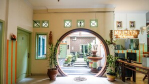 Un pasillo con un espejo grande que refleja un patio con una fuente, plantas en macetas y un letrero que dice "NARITA Wisma".