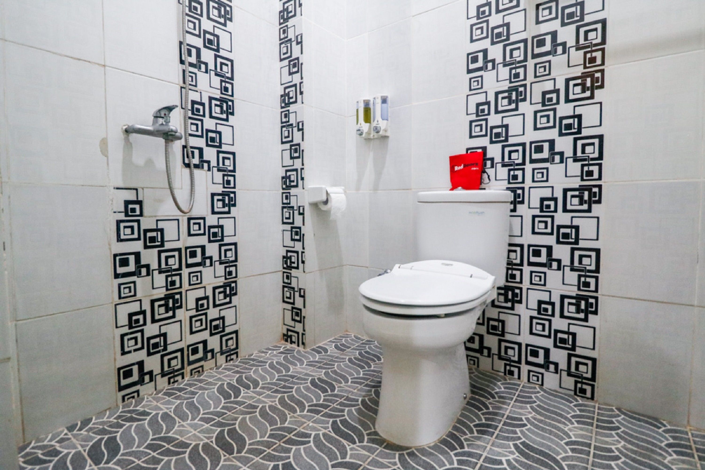 Et badeværelse med toilet, bruser og tapetserede fliser.
