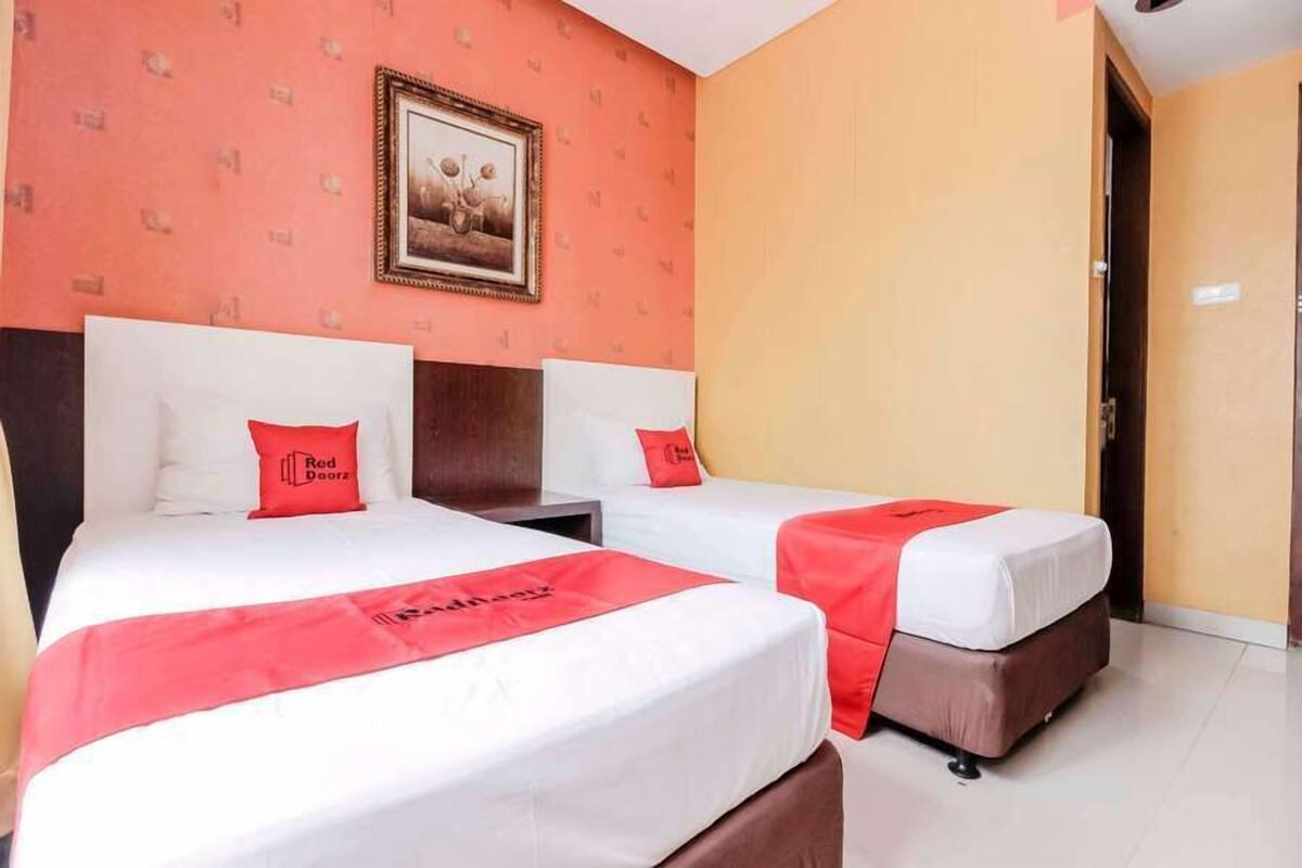 A hotel room with two beds, each with a red accent pillow and a red bedspread.