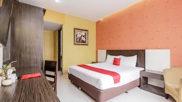 A hotel room with a large bed, a wooden desk, a chair, a small table, and a potted plant.