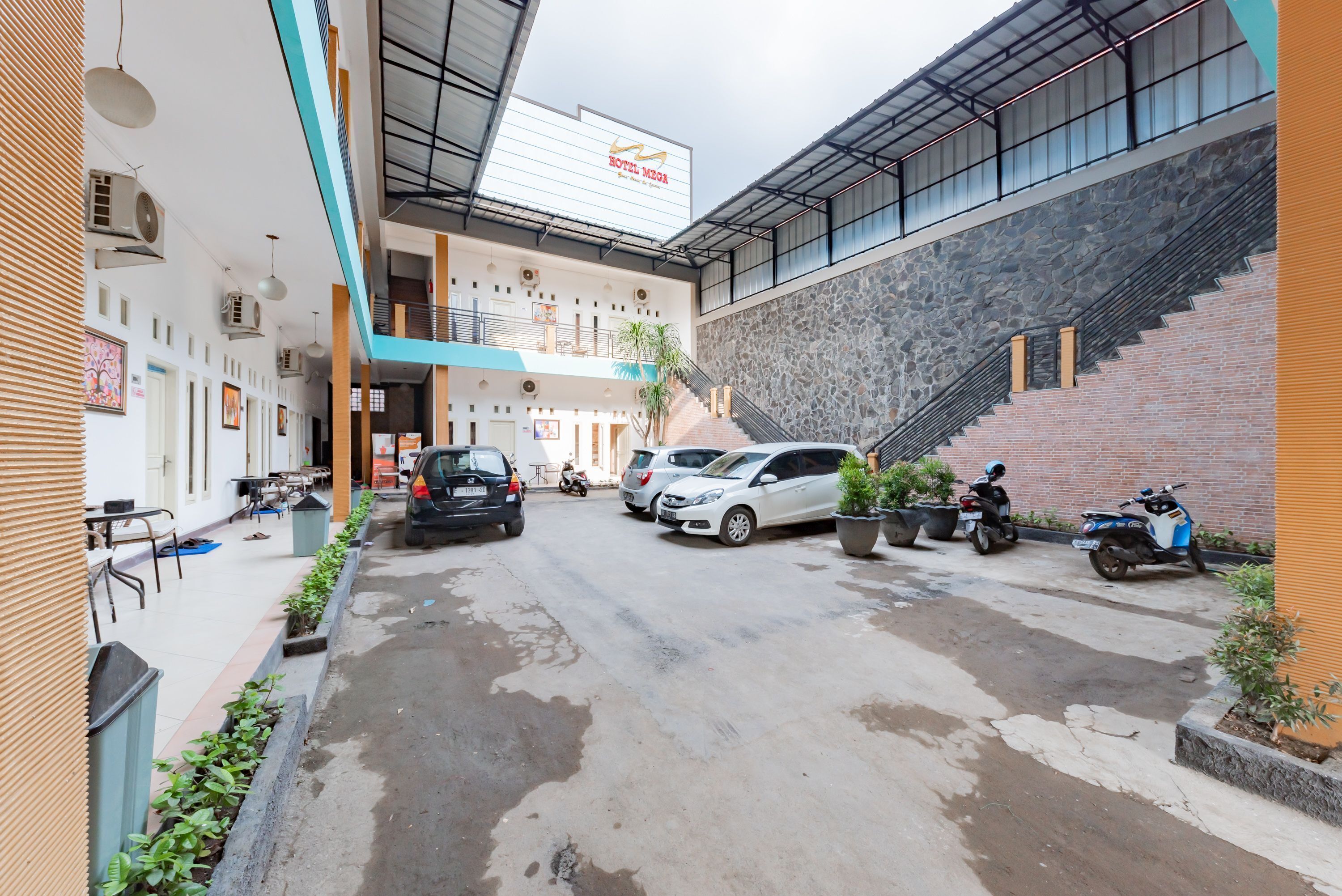 A hotel courtyard with a covered walkway, parked cars, and a staircase leading to an upper level.