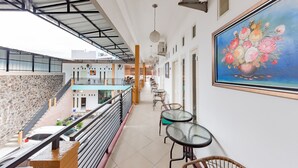 A corridor with a view of the street, a staircase, and a painting of flowers on the wall.