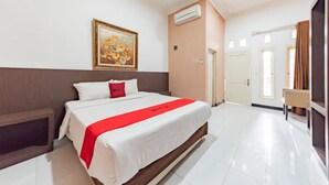 A hotel room with a large bed, a painting on the wall, an air conditioning unit, and a door leading to another room.
