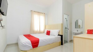 A hotel room with a bed, a bedside table, a mirror, a shower, and a sink.