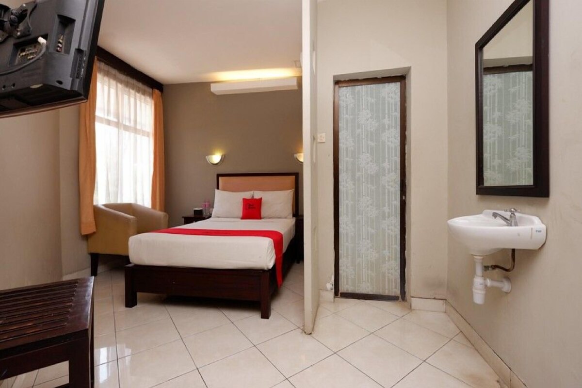 A hotel room with a bed, a chair, a television, and a bathroom with a sink and mirror.