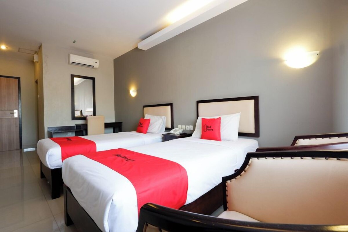 A hotel room with two beds, a desk, a chair, and a mirror.