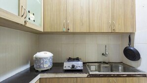 Uma cozinha compacta com armários de madeira, panela de arroz, fogão a gás, pia e uma frigideira pendurada.