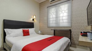 Quarto de hotel com cama, mesa de cabeceira, escrivaninha, lareira e janela com persiana decorativa.