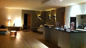 A modern living room with a sofa, a coffee table, and a small table with a lamp. There is a kitchen area with a counter and a refrigerator. - House / Villa - Poggio d''oletta (Poggio-D'oletta)