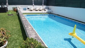 Ein rechteckiger Swimmingpool mit klarem, blauen Wasser, umgeben von einer Betonplattform und einer Rasenfläche mit Blumentöpfen.
