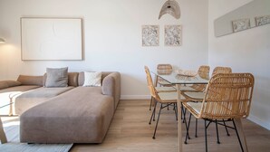 A modern living room with a sofa, dining table, wicker chairs, and artwork on the walls. - Three bedroom apartment with balcony in Ali Bei - You Stylish (Barcelona)
