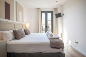Ein Hotelzimmer mit einem Bett, einem an der Wand montierten Fernseher und einem Fenster mit Vorhängen.