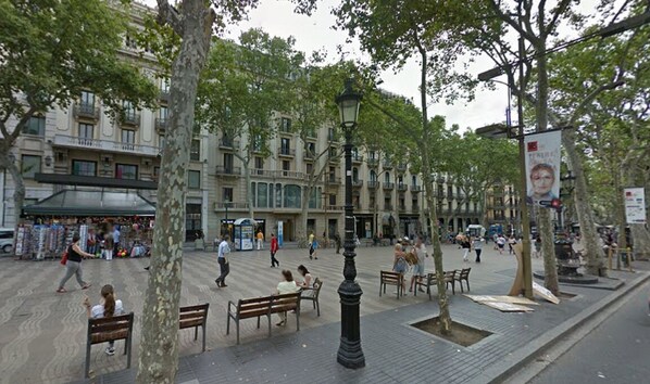 A public square with benches, trees, and a few people walking.