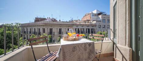 Un balcón con una mesa dispuesta para el desayuno, una silla y vistas de edificios al fondo.