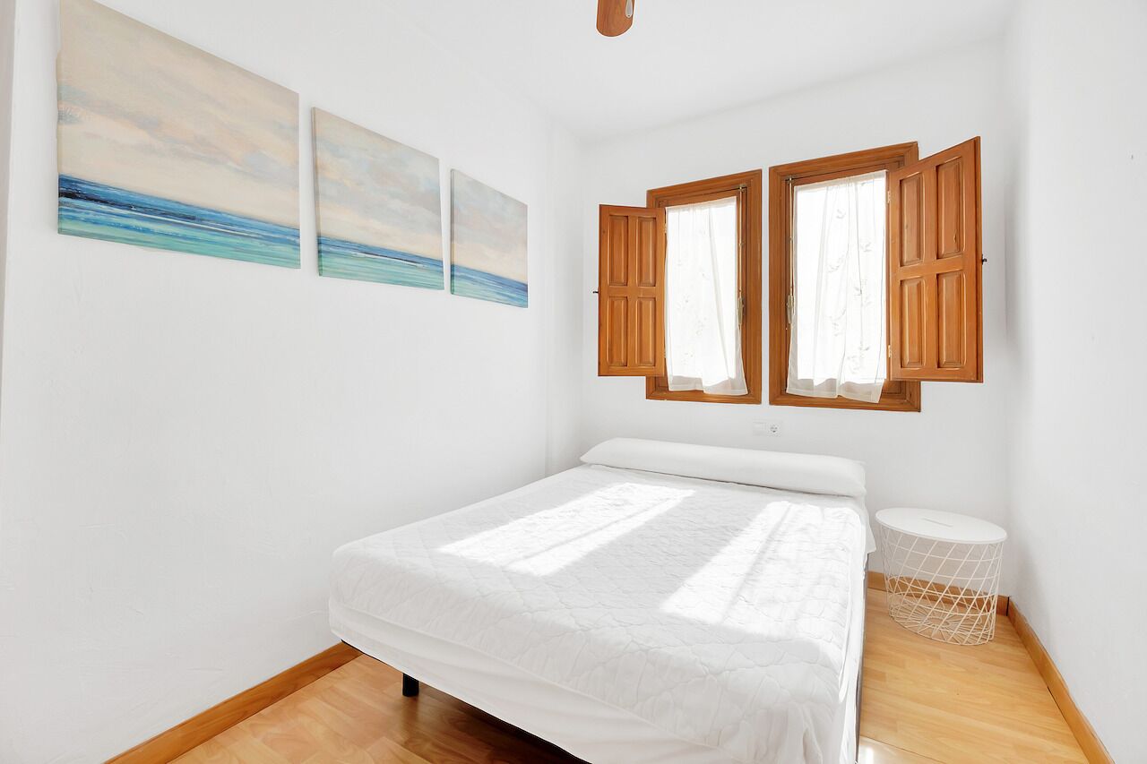 A bedroom with a bed, two windows with wooden shutters, and three wall-mounted paintings.