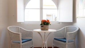 Zwei weiße Korbstühle mit blauen Kissen um einen kleinen, weißen Tisch, auf dem ein geflochtener Korb mit orangefarbenen Blumen steht.
