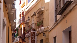 Eine schmale Gasse mit Tischen, Stühlen, Pflanzkübeln und einem großen Fass.