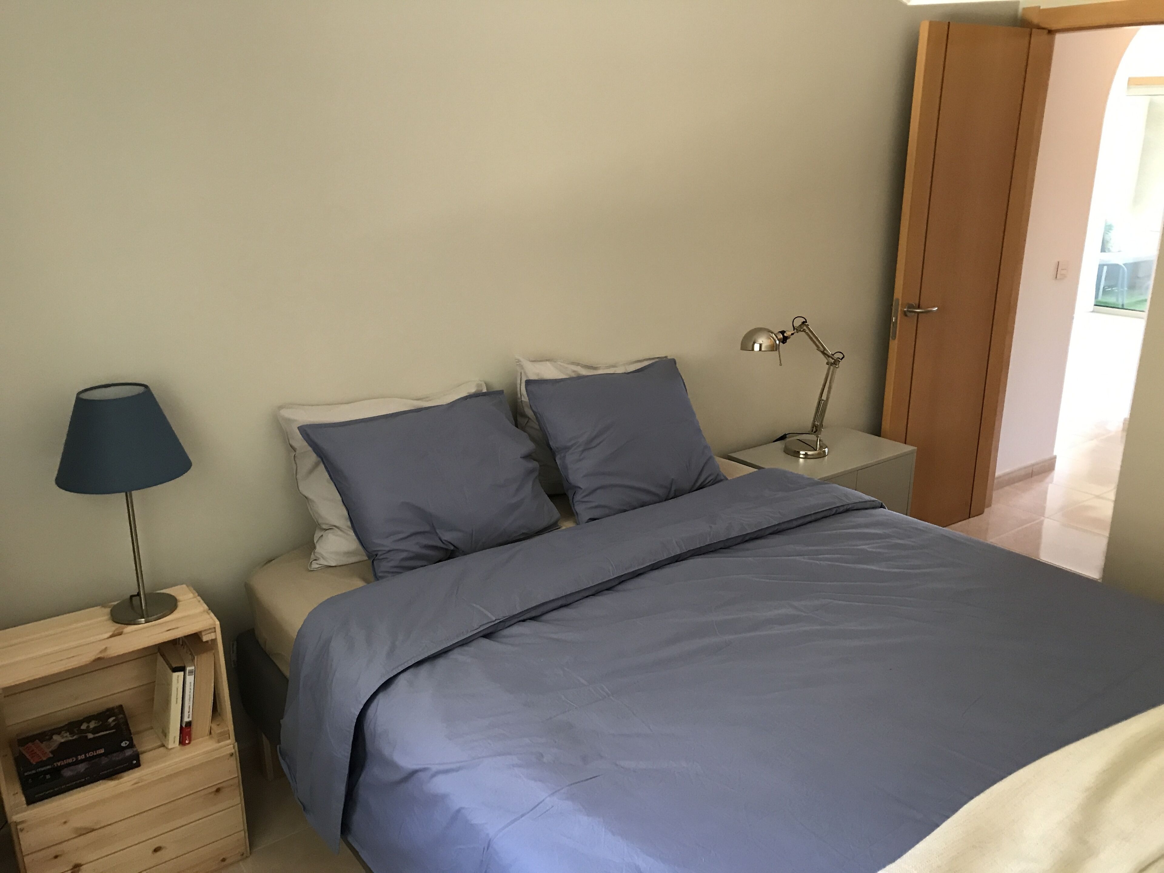 Una camera da letto con un letto, un comodino con una lampada e una mensola in legno con dei libri.