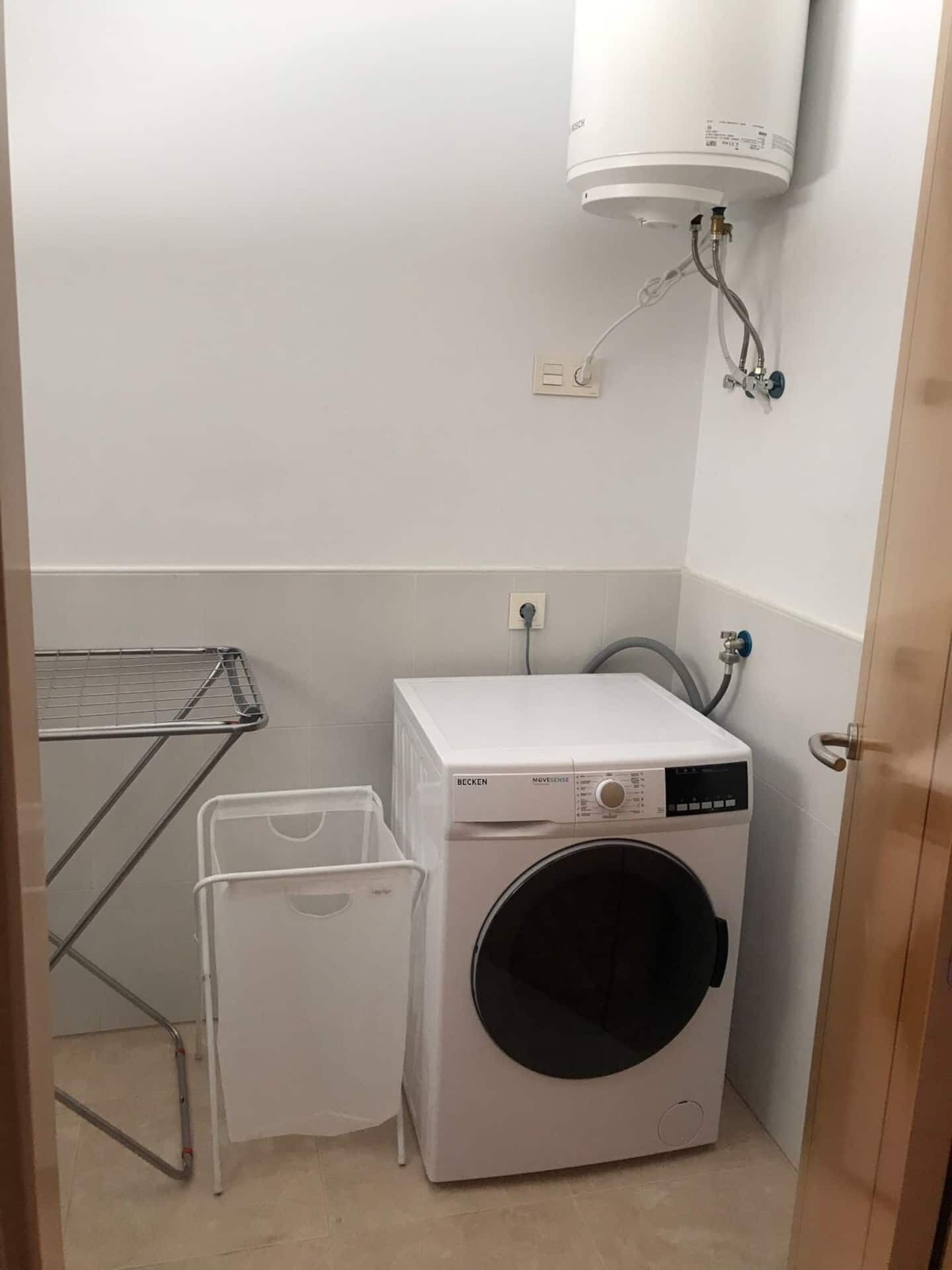 Une petite buanderie équipée d’un lave-linge à chargement frontal, d’un sèche-linge et d’un chauffe-eau mural.