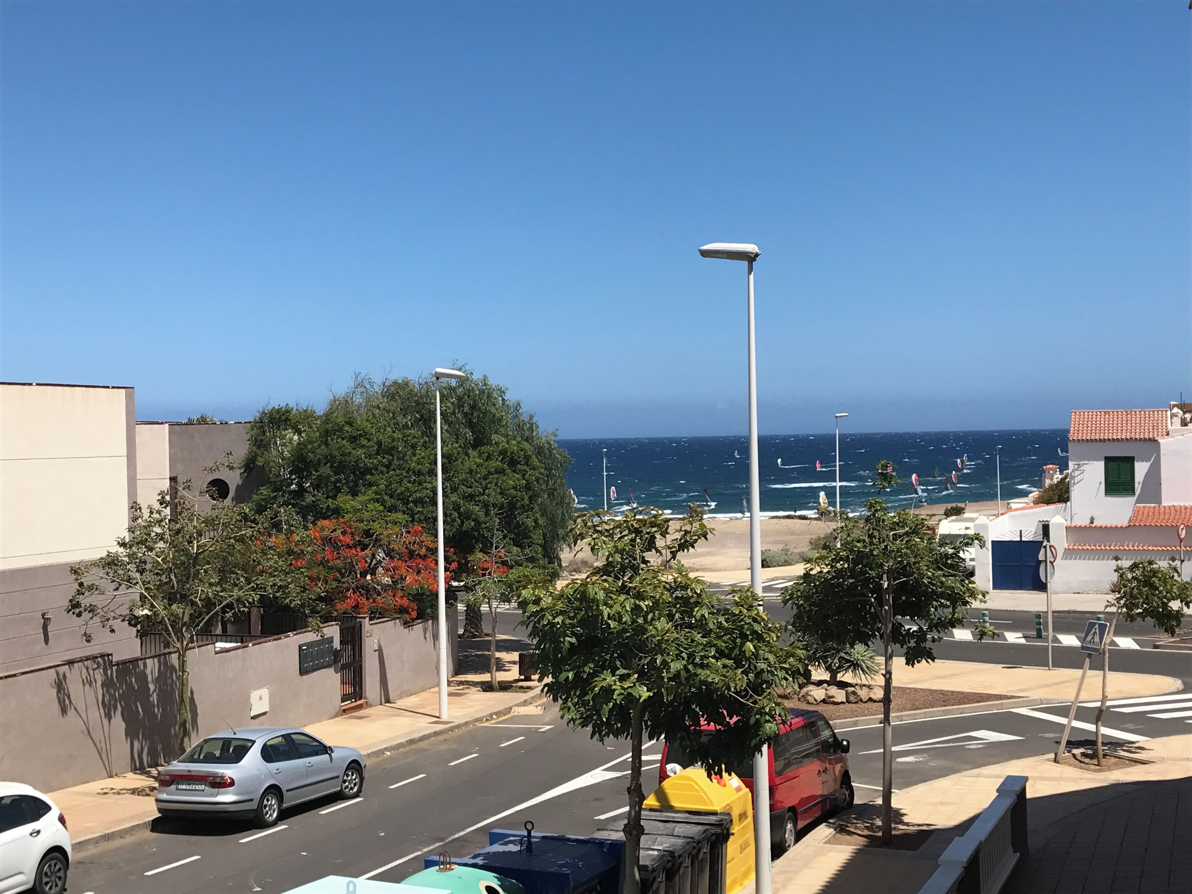 Eine Küstenstraße mit freiem Blick auf den Ozean, ein rotes Lieferwagen am Straßenrand und ein weißes Auto im Vordergrund.