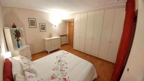 Een slaapkamer met een bed, een dressoir, een kledingkast en een spiegel met een vaas.