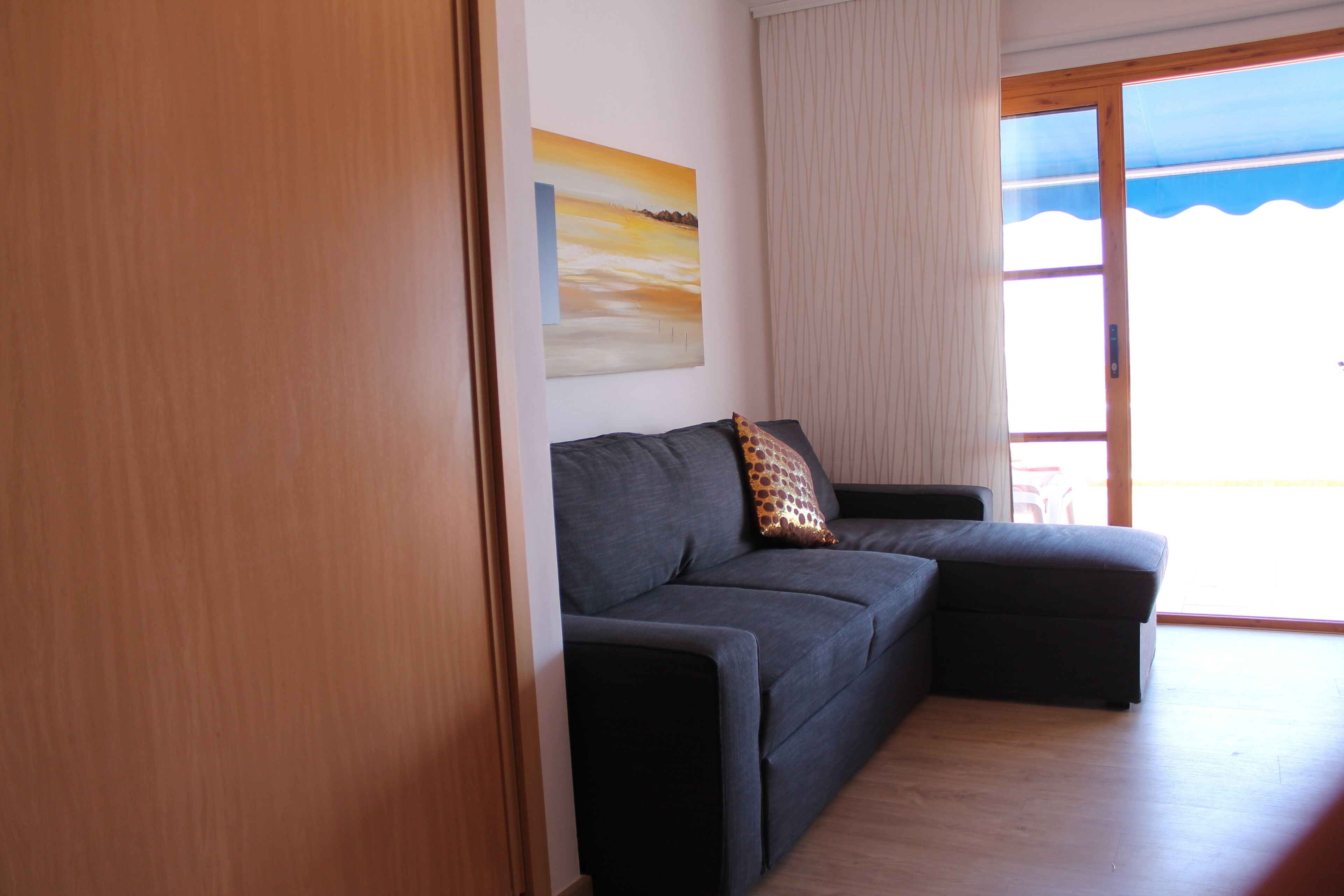 Ein modernes Wohnzimmer mit einem dunkelgrauen Sofa, Holzboden, einem großen Fenster mit Aussicht und einem Bild an der Wand.