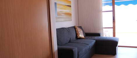 Ein modernes Wohnzimmer mit einem dunkelgrauen Sofa, Holzboden, einem großen Fenster mit Aussicht und einem Bild an der Wand.