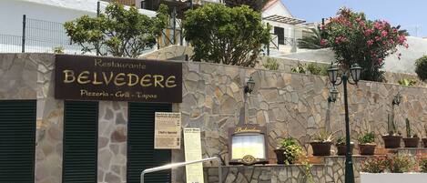 A restaurant named Belvedere with a stone facade, green shutters, and outdoor seating with potted plants.