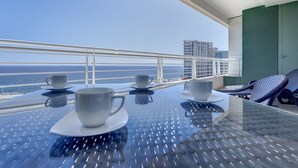 A balcony with a table set for two, two cups, and a view of the ocean and buildings. - Seafront Lux Fort Cambridge wt Pool (Sliema)