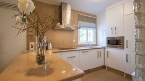 Une cuisine moderne avec des meubles blancs, un four à micro-ondes en acier inoxydable et un vase rempli de fleurs posé sur le plan de travail.