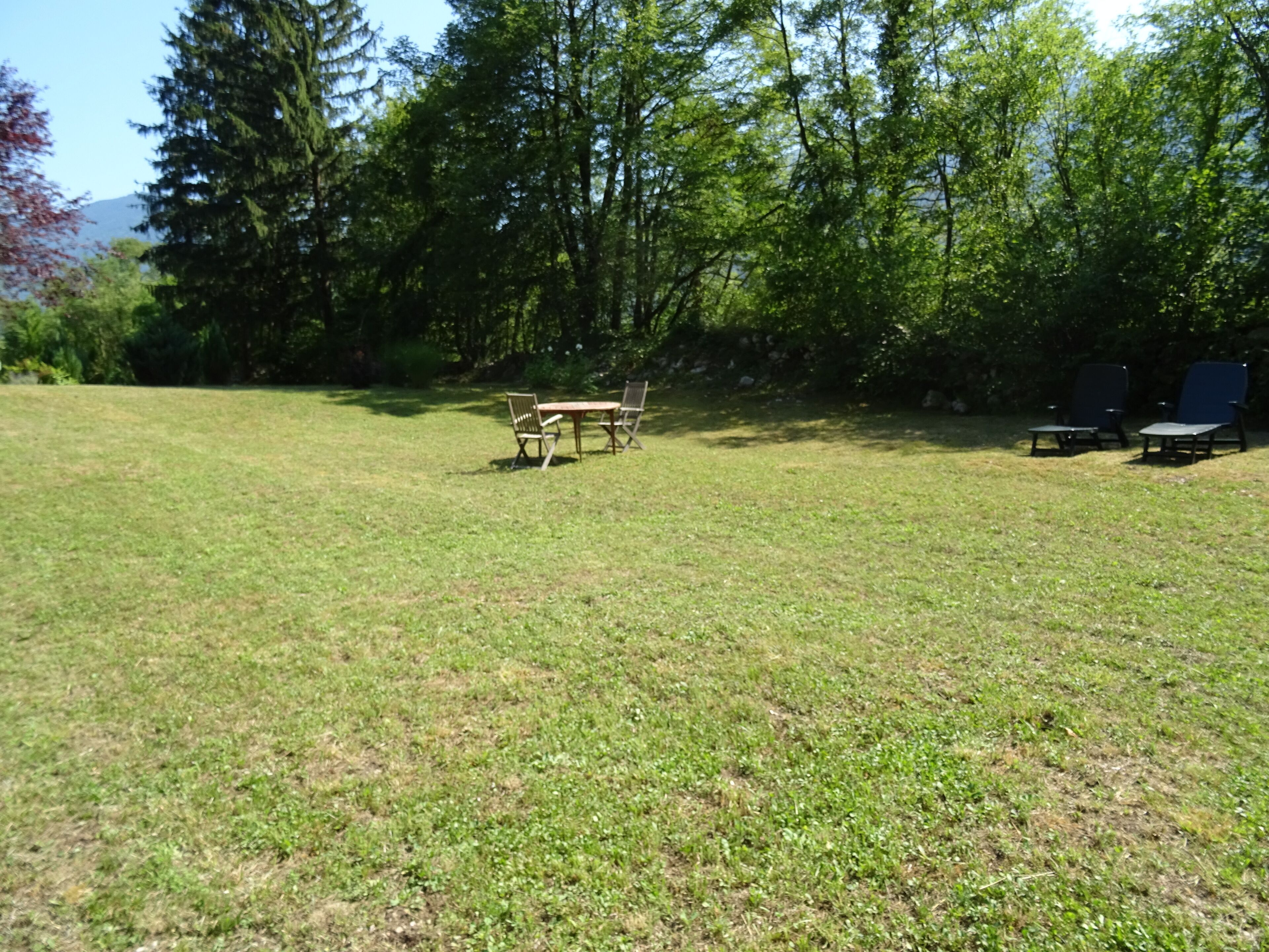 An outdoor area with a grassy lawn, a wooden table, and two chairs.