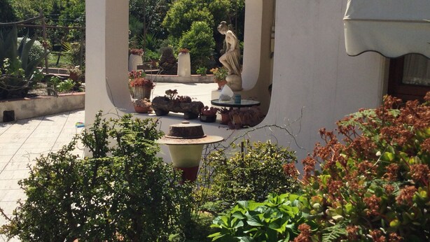 Un patio al aire libre con una estatua, plantas en macetas y una mesa de piedra.
