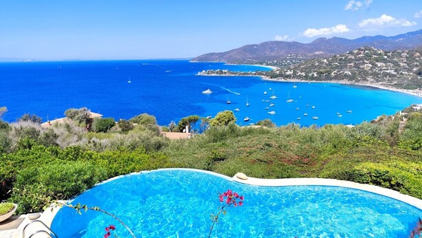 On aperçoit clairement une piscine, avec la mer en toile de fond et un paysage montagneux à l’horizon.