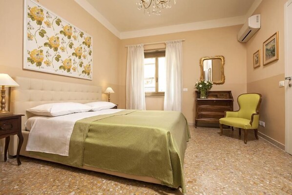 Een hotelkamer met een bed, een stoel, een dressoir, een spiegel en een raam met gordijnen.