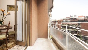 Varanda com vista para edifícios vizinhos, porta de correr de vidro e uma pequena mesa com cadeiras.