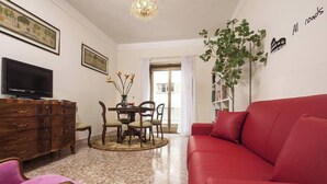 Uma sala de estar com um sofá vermelho, uma TV em um armário de madeira, uma mesa de jantar com cadeiras e um vaso de planta.