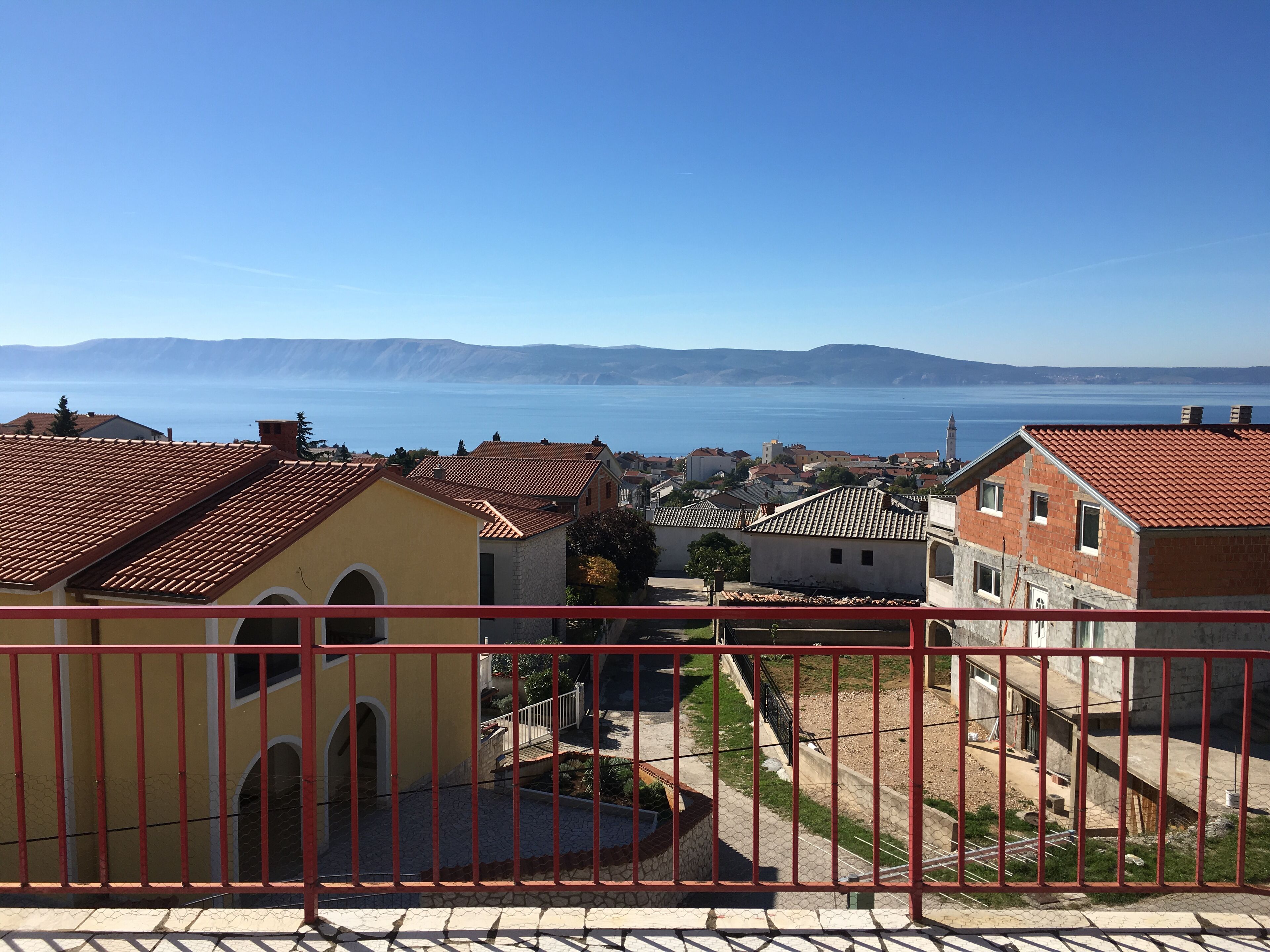 Eine Küstenstadt mit terrakottafarbenen Dächern, einem klaren blauen Meer und fernen Bergen.