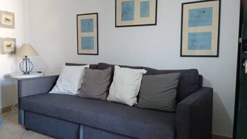 Una sala de estar con un sofá gris, una mesita auxiliar con una lámpara y tres cuadros en la pared.