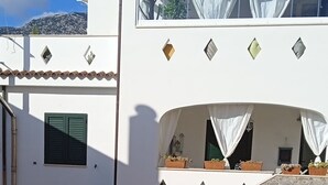 Un bâtiment blanc avec un escalier en pierre, un petit jardin agrémenté de plantes en pot et une clôture en bois.